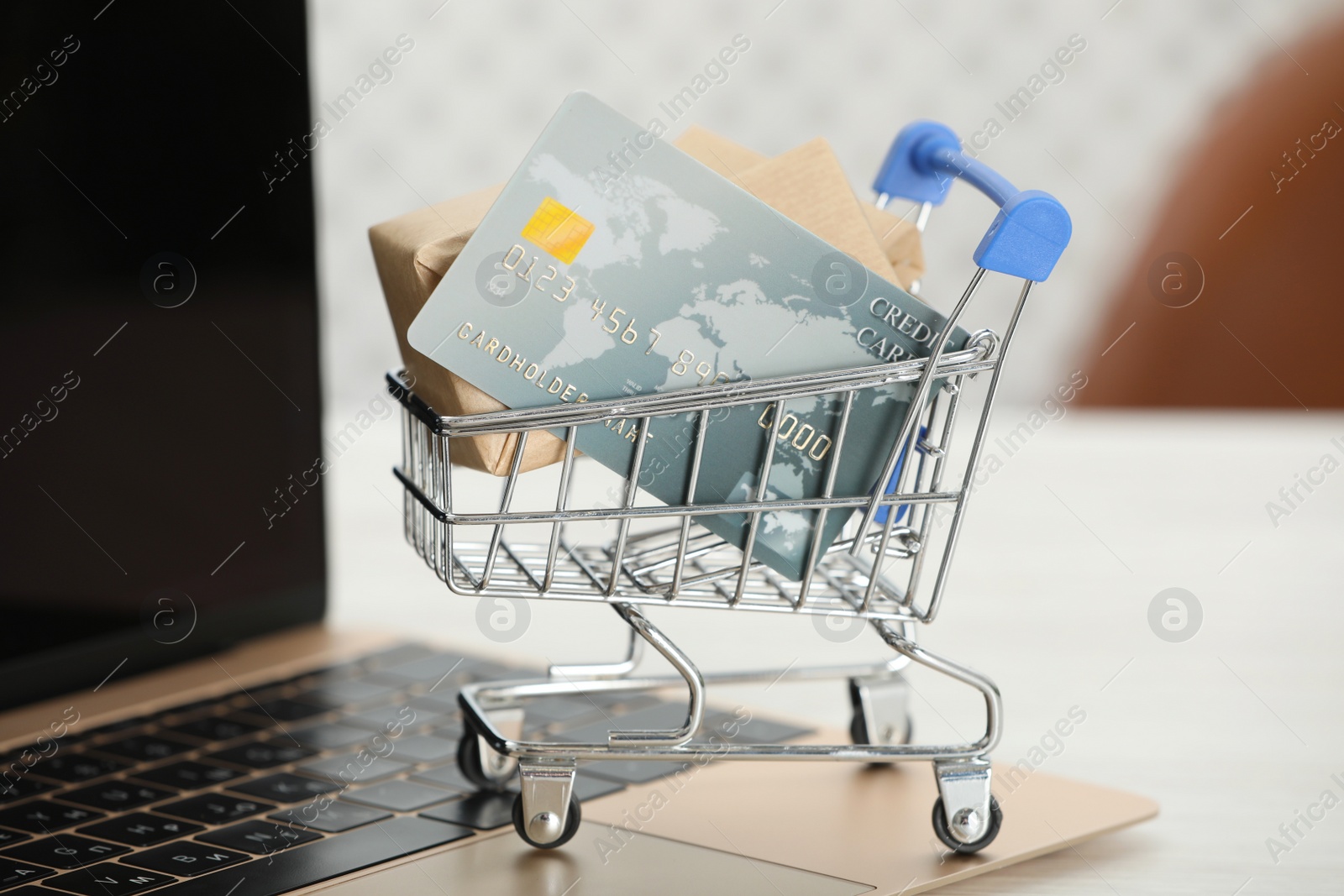 Photo of Online payment concept. Small shopping cart with bank card, boxes and laptop on white table, closeup