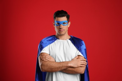 Man wearing superhero cape and mask on red background