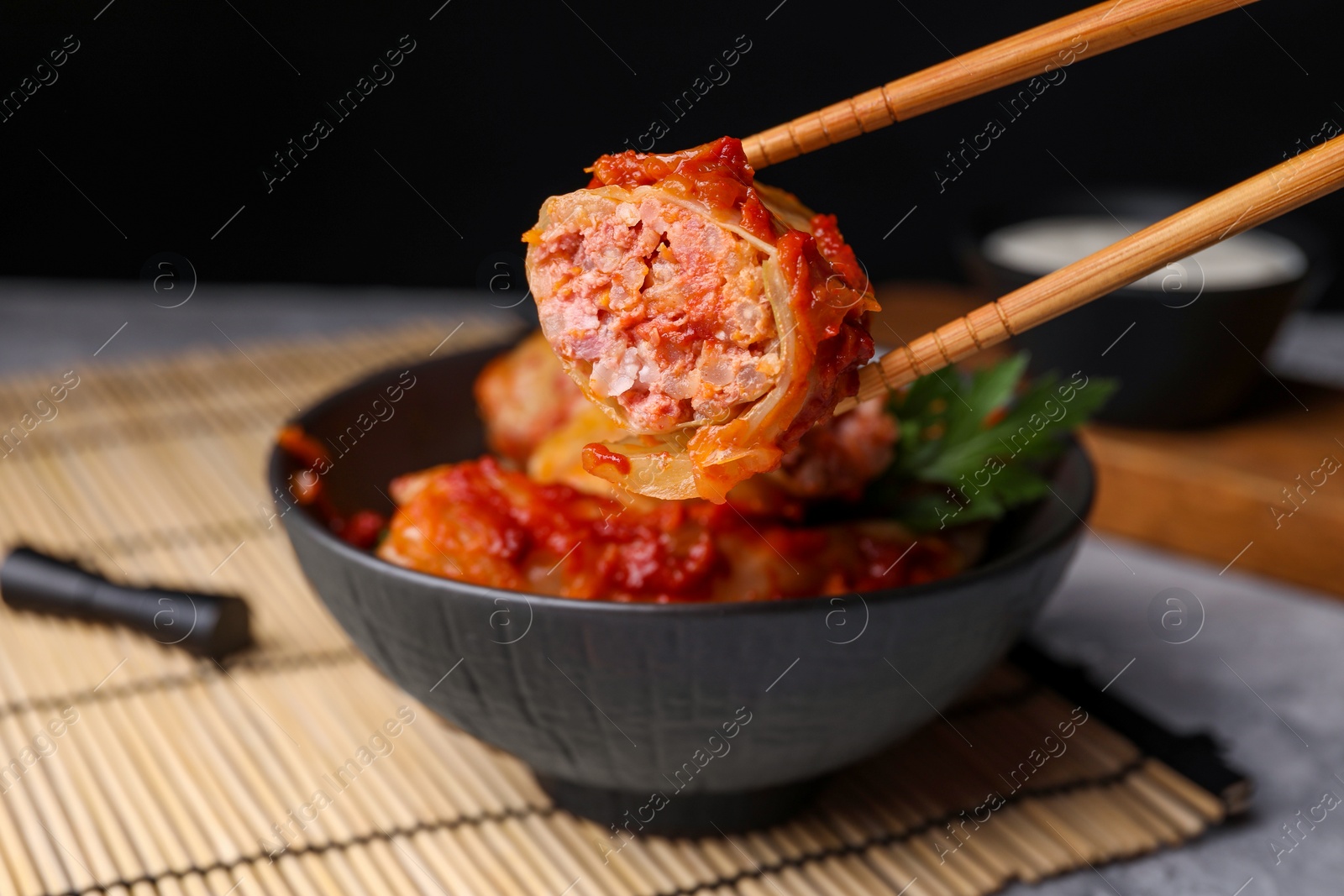 Photo of Taking delicious stuffed cabbage roll from bowl at table, closeup
