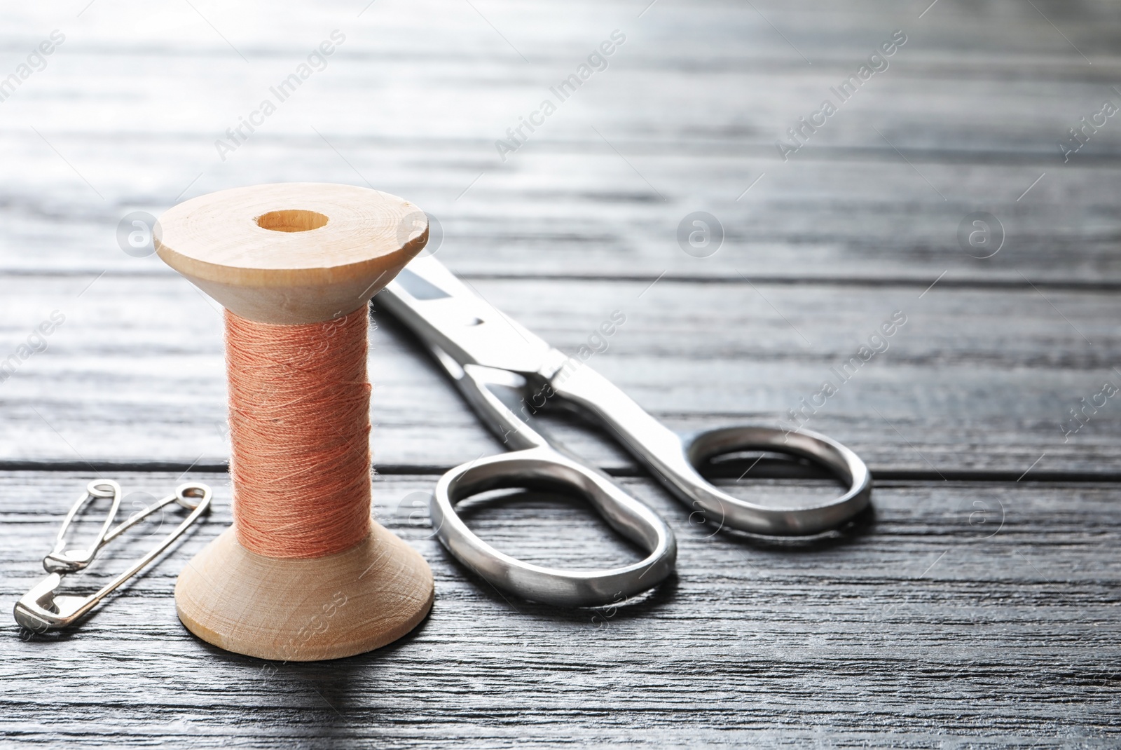 Photo of Spool of thread, scissors and pins on wooden background. Tailoring equipment