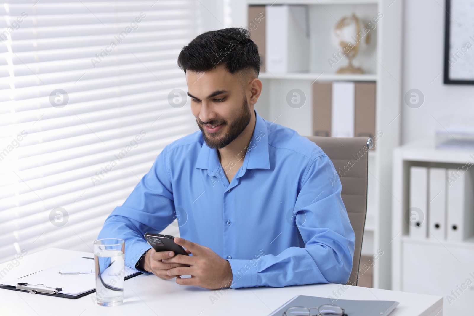 Photo of Handsome young man using smartphone at white table in office