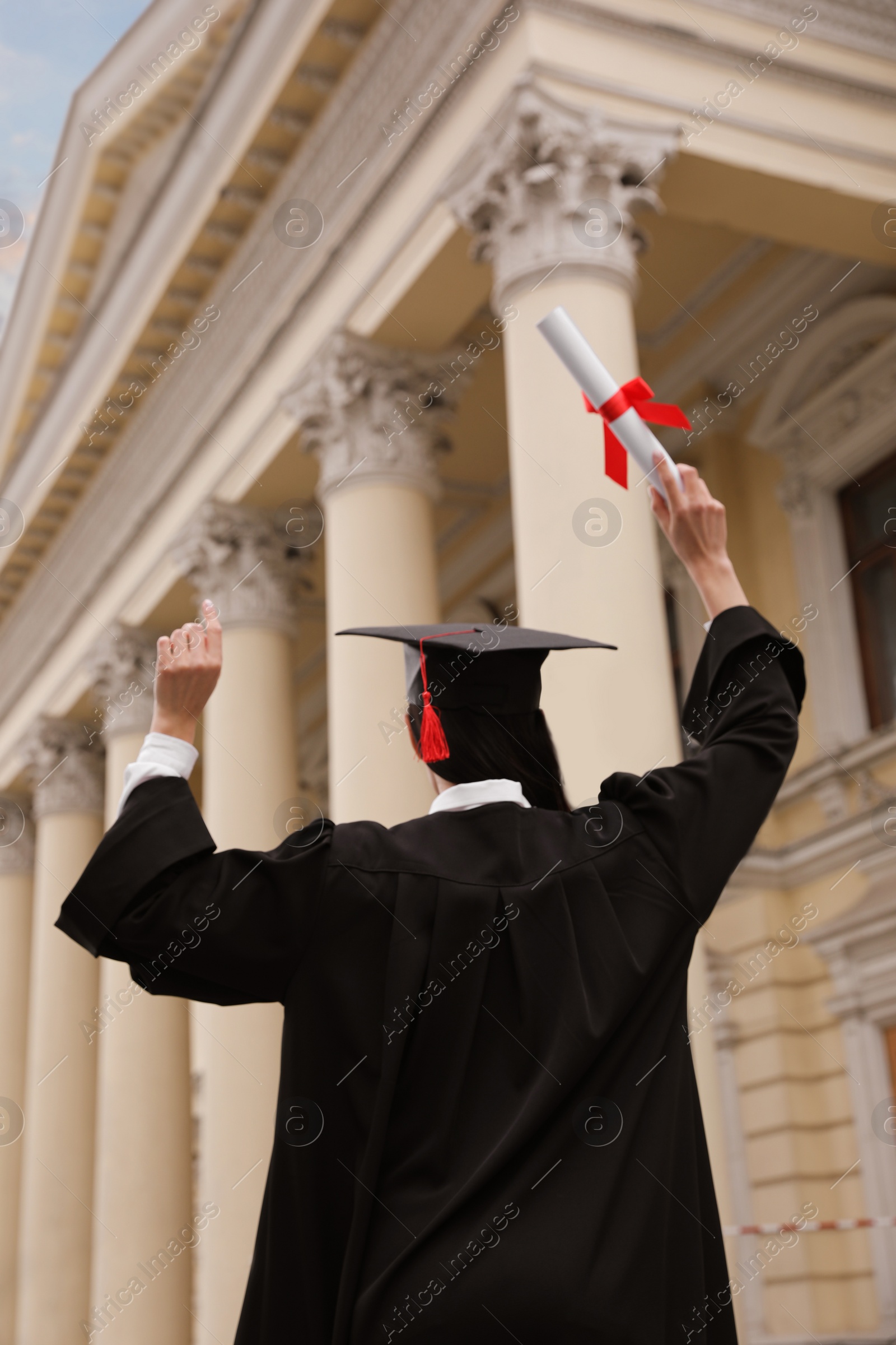 Photo of Student with diploma after graduation ceremony outdoors, back view