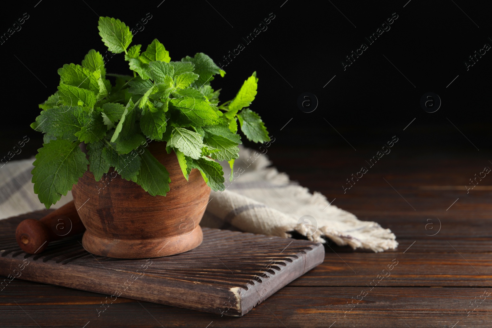 Photo of Mortar fresh green lemon balm leaves on wooden table. Space for text