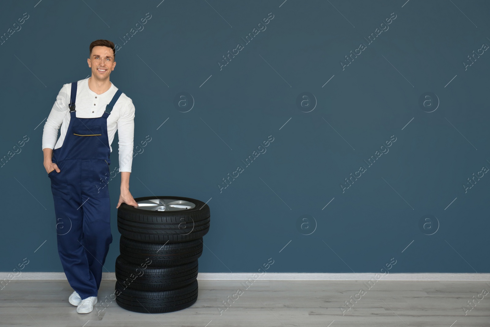 Photo of Male mechanic with car tires on grey wall background