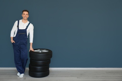 Male mechanic with car tires on grey wall background