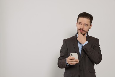 Pensive man in suit with smartphone against light grey background. Space for text