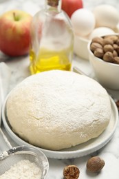 Photo of Raw dough, nutmeg seeds and other ingredients for pastry on white marble table, closeup