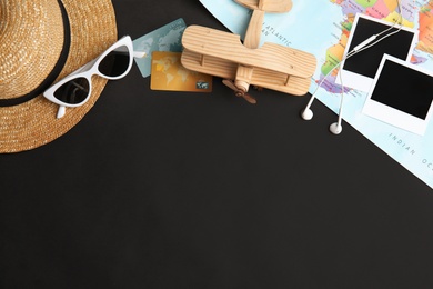 Photo of Flat lay composition with tourist items and airplane on black background, space for text. Travel agency