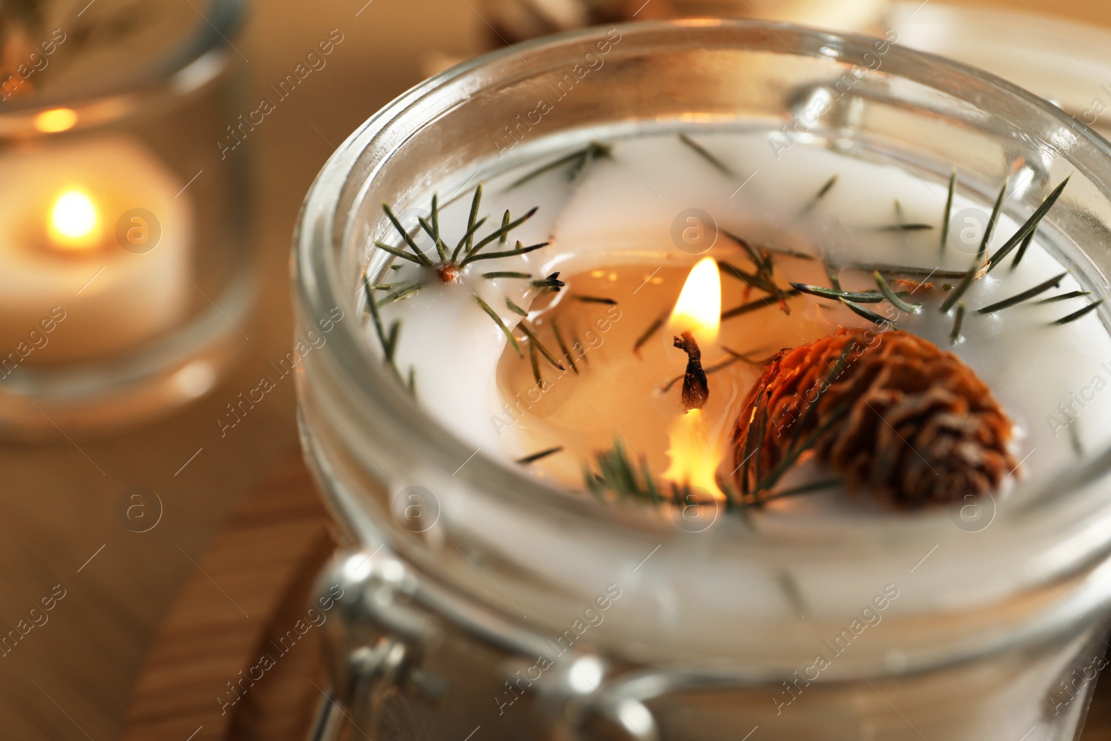 Photo of Burning scented conifer candle in glass jar, closeup view