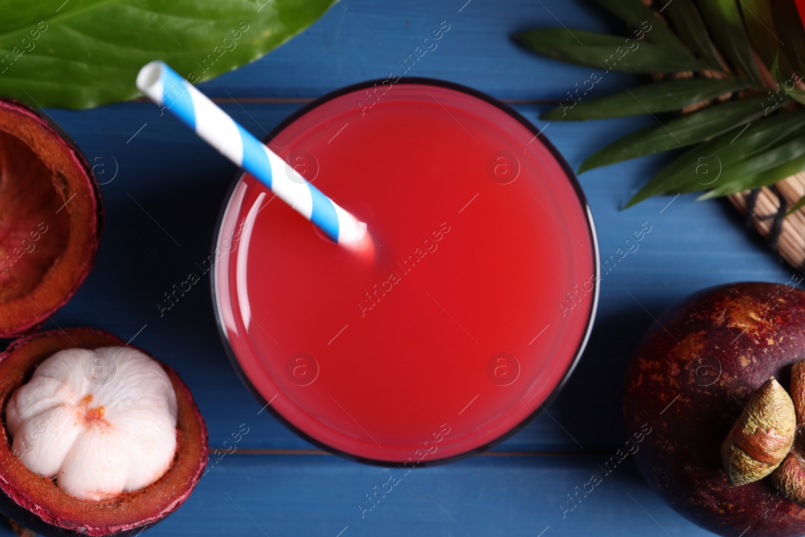 Photo of Delicious mangosteen juice and fresh fruits on blue wooden table, flat lay