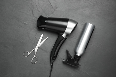 Photo of Hair dryer and professional hairdresser tools on black background, flat lay