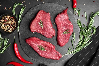 Photo of Fresh raw meat steaks and spices on black table, flat lay