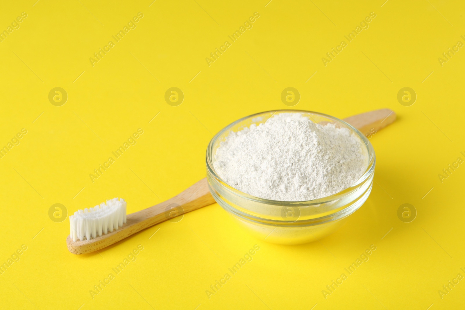 Photo of Bowl of tooth powder and brush on yellow background