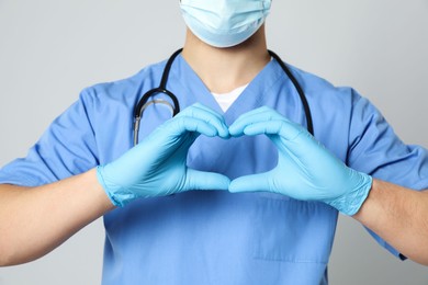 Photo of Doctor or medical assistant (male nurse) with stethoscope making heart on light grey background, closeup