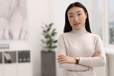 Portrait of smiling businesswoman with crossed arms in office. Space for text