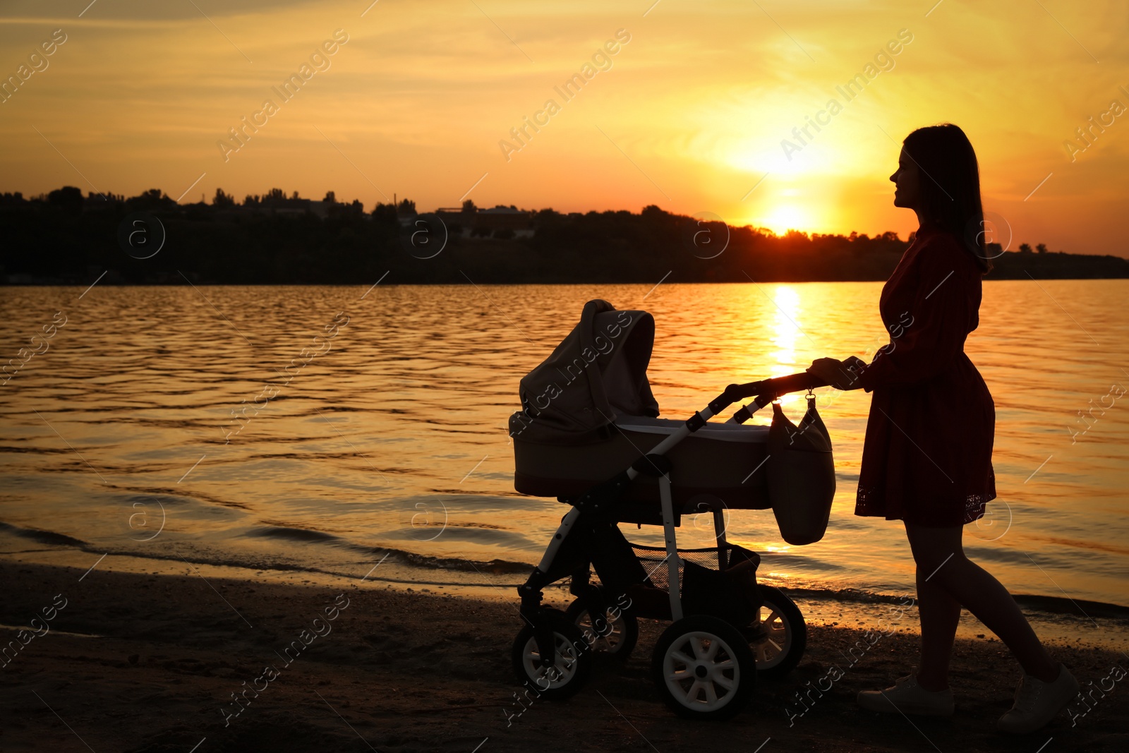 Photo of Happy mother with baby in stroller walking near river at sunset