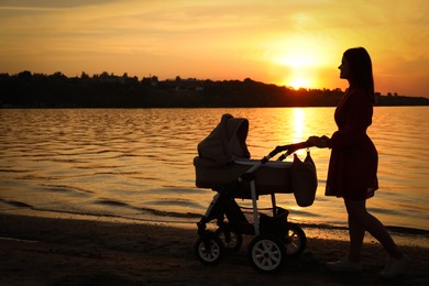 Happy mother with baby in stroller walking near river at sunset