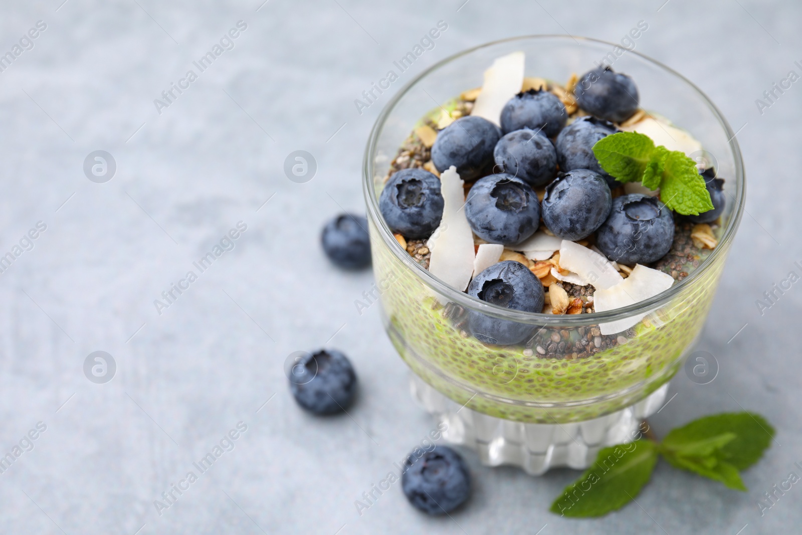 Photo of Tasty chia matcha pudding with coconut and blueberries on grey table, space for text. Healthy breakfast