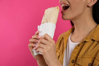 Photo of Young woman eating delicious shawarma on pink background, closeup