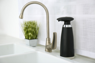 Photo of Modern automatic soap dispenser near sink in kitchen