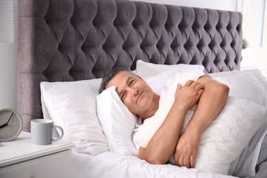 Photo of Happy man waking up after sleeping on comfortable pillow in bed at home