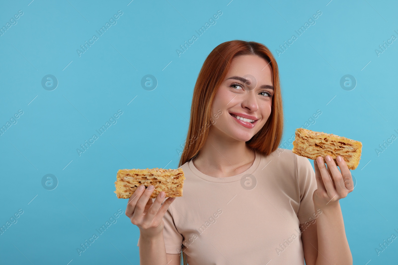 Photo of Young woman with pieces of tasty cake on light blue background, space for text