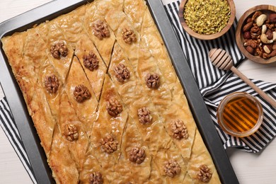 Photo of Delicious baklava with walnuts in baking pan, honey and nuts on white wooden table, flat lay
