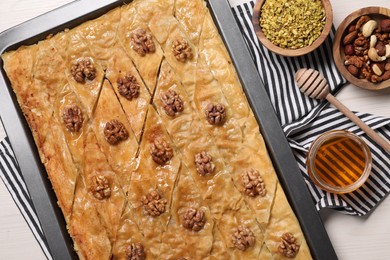 Delicious baklava with walnuts in baking pan, honey and nuts on white wooden table, flat lay