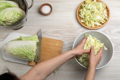 Photo of Woman putting cut Chinese cabbage into bowl at white wooden kitchen table, top view