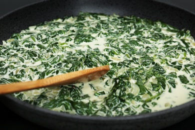 Photo of Tasty spinach dip with wooden spoon in frying pan, closeup view