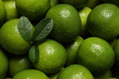 Photo of Fresh ripe limes and leaves with water drops as background, top view