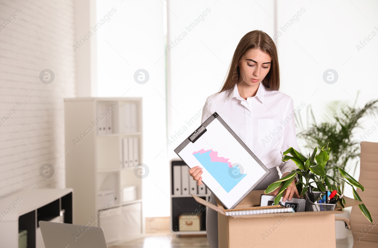 Photo of Upset young woman packing stuff in box at office