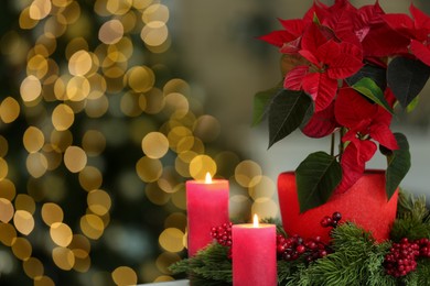 Photo of Potted poinsettia, burning candles and festive decor in room, closeup with space for text. Christmas traditional flower