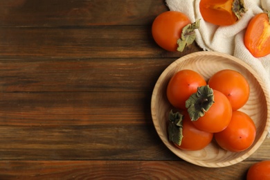 Tasty ripe persimmons on wooden table, flat lay. Space for text