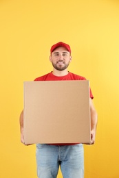 Portrait of man in uniform carrying carton box on color background. Posture concept