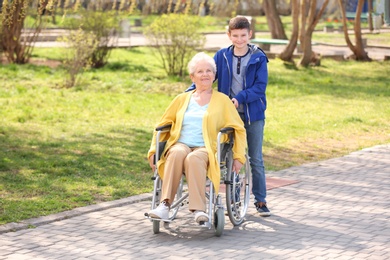 Senior woman in wheelchair with her grandson on sunny day outdoors
