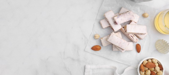 Image of Pieces of delicious nutty nougat and ingredients on white marble table, flat lay. Banner design with space for text