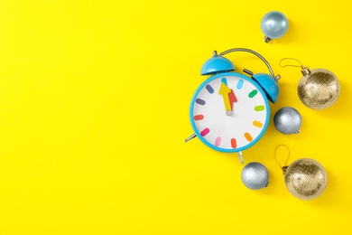 Photo of Alarm clock and festive decor on yellow background, flat lay with space for text. New Year countdown
