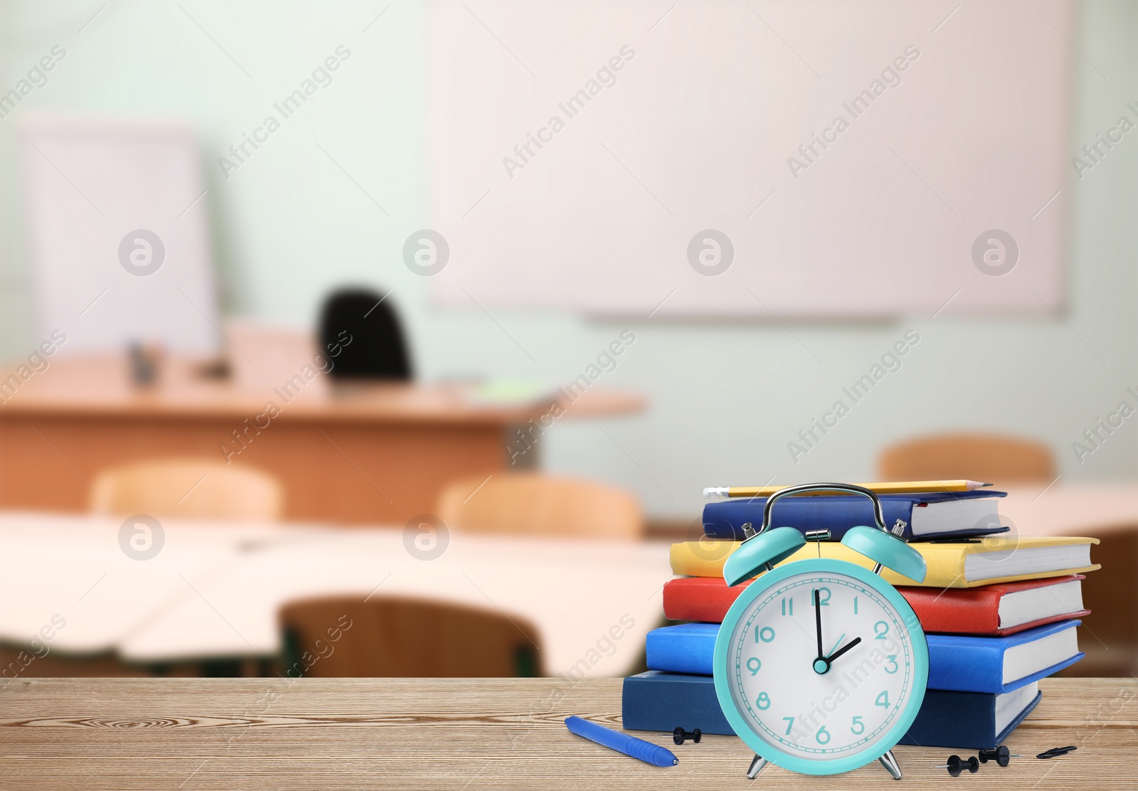 Image of Turquoise alarm clock and different stationery on wooden table in classroom, space for text