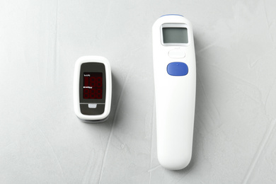 Photo of Modern fingertip pulse oximeter and non contact infrared thermometer on light grey stone background, flat lay