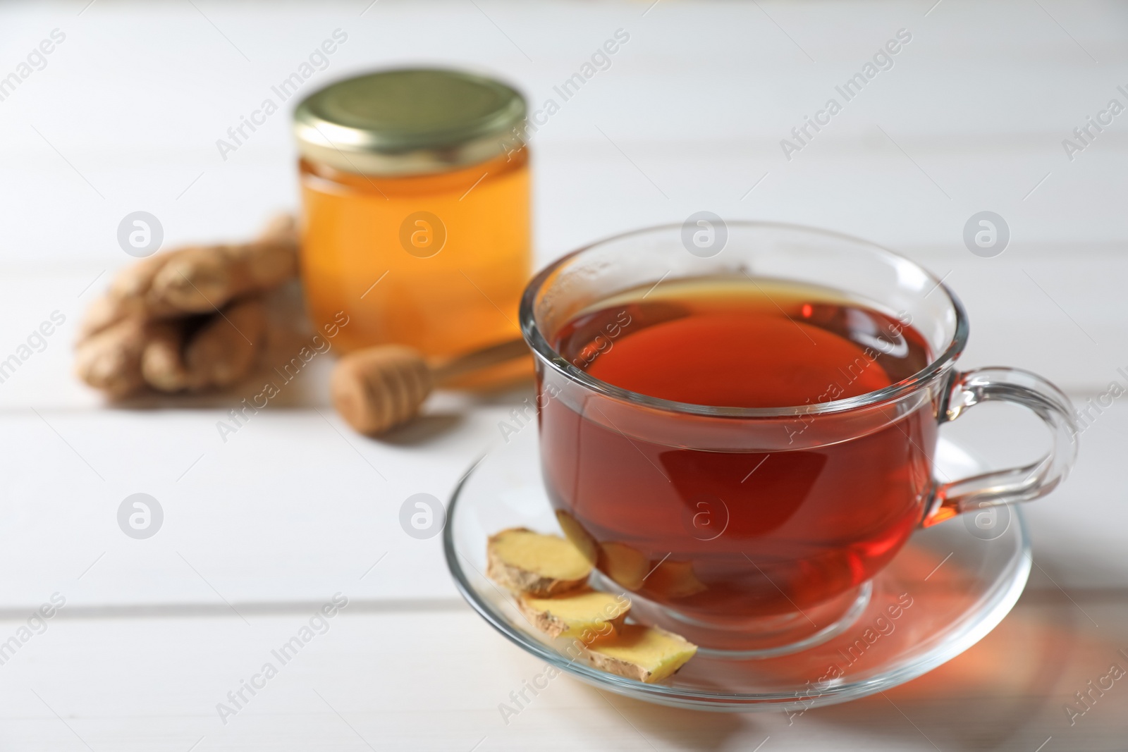 Photo of Cup of delicious ginger tea and ingredients on white wooden table, closeup. Space for text