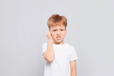 Little boy suffering from ear pain on light grey background