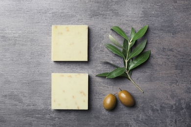 Photo of Handmade soap bars and leaves with olives on grey background, top view