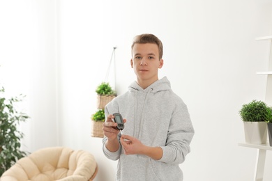 Teen boy holding digital glucometer at home. Diabetes control