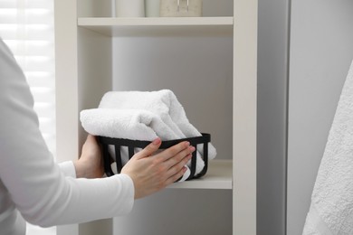 Woman stacking clean towels on shelf in bathroom, closeup