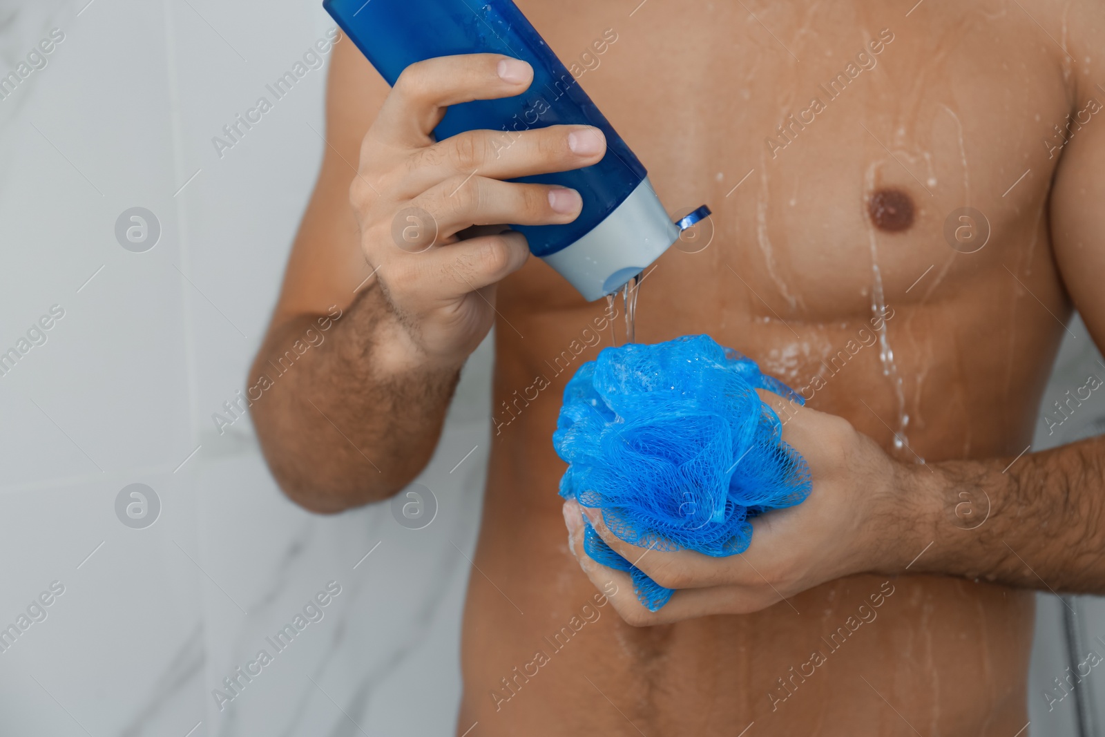 Photo of Man applying gel onto mesh pouf in shower at home, closeup