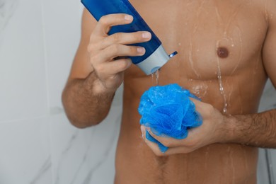 Photo of Man applying gel onto mesh pouf in shower at home, closeup