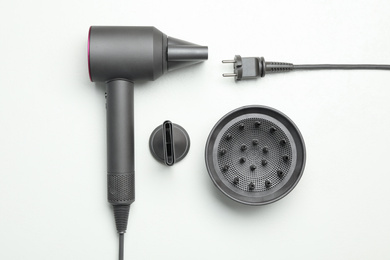 Hair dryer with different attachments on white table, flat lay. Professional hairdresser tool