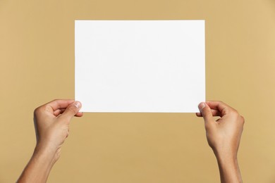 Man holding sheet of paper on beige background, closeup. Mockup for design