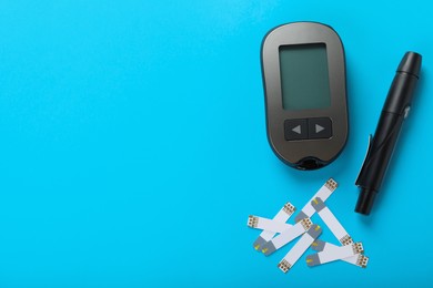 Photo of Digital glucometer, lancet pen and test strips on light blue background, flat lay with space for text. Diabetes control
